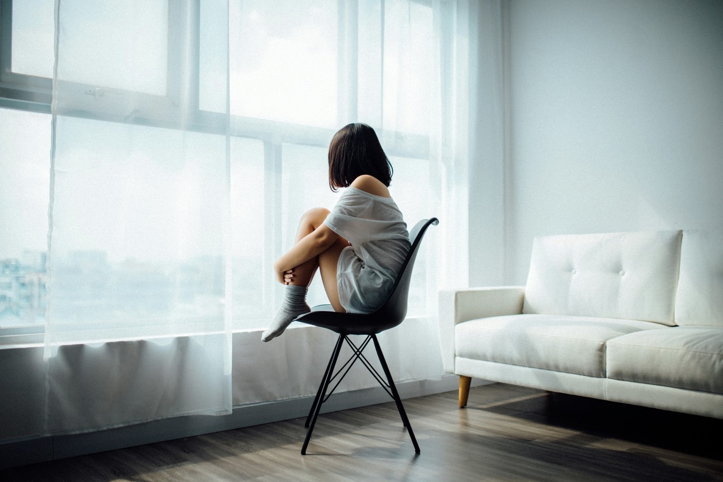 Image on lone woman sitting in a chair facing a window